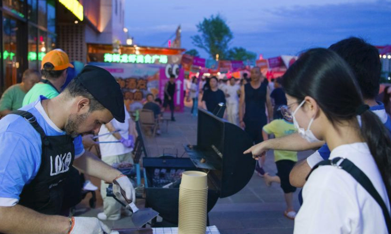 Gabriel Martin (1st L) cooks steaks during a beer festival in the ancient city of Wuhu in Wuhu City, east China's Anhui Province, July 19, 2024. (Xinhua/Zhang Duan)