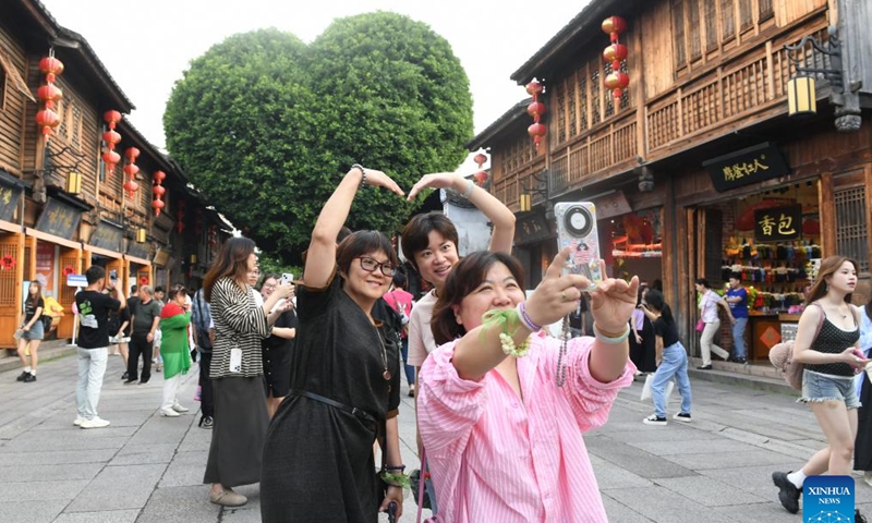 Tourists pose for selfies in front of a heart-shaped tree on a street in the ancient Sanfangqixiang (Three Lanes and Seven Alleys) area in Fuzhou, southeast China's Fujian Province, June 7, 2024.