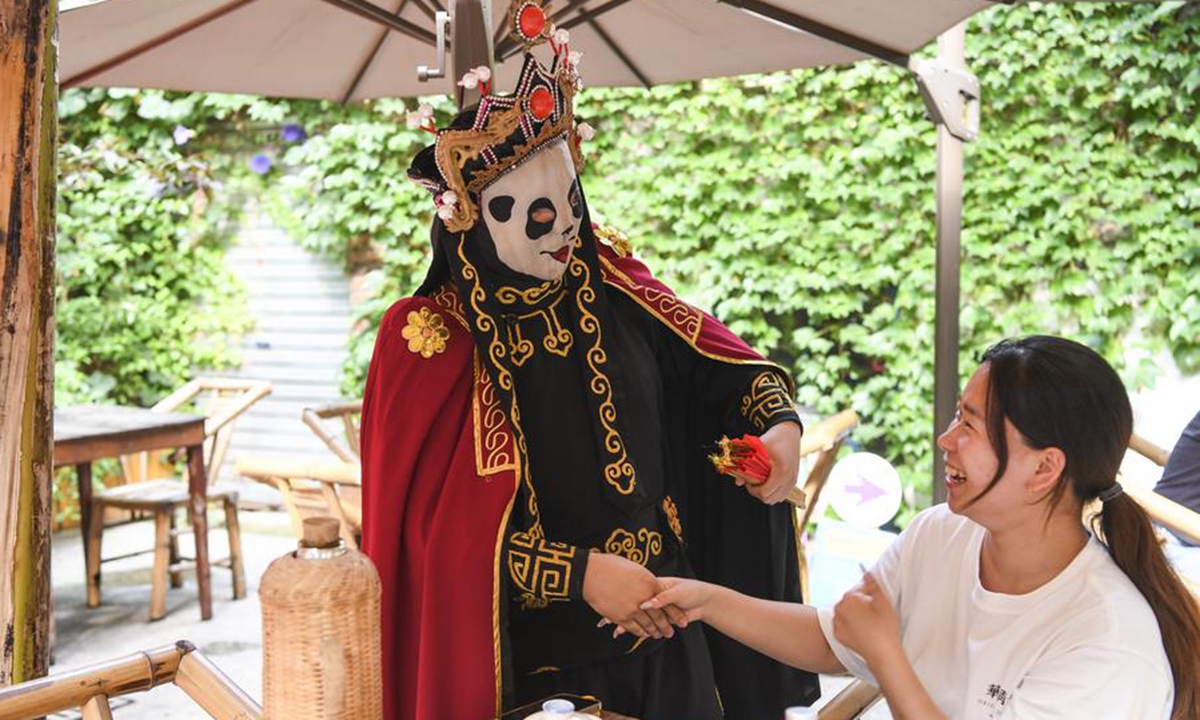 A tourist interacts with an actor performing face-changing of Sichuan Opera at an open-air teahouse in Shancheng Alley in Yuzhong District, southwest China's Chongqing Municipality, May 30, 2024. (Xinhua/Wang Quanchao)
