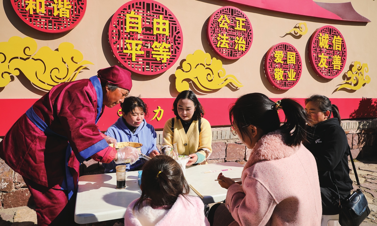 A villager from Songjiagou (in red) severs tourists with local special cuisine. Photo: Courtesy of China Rural Revitalization magazine