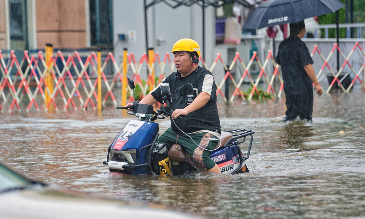 A local resident in Zhengzhou, Central China's Henan Province, struggles to ride through a flooded street on July 8, 2024. The Henan provincial meteorological bureau announced the launch of a Level IV emergency response to a major meteorological disaster (heavy rain). From July 7 to 8, a total of 78 warnings for heavy rain, strong winds, and thunderstorms have been issued across the province. Photo: VCG