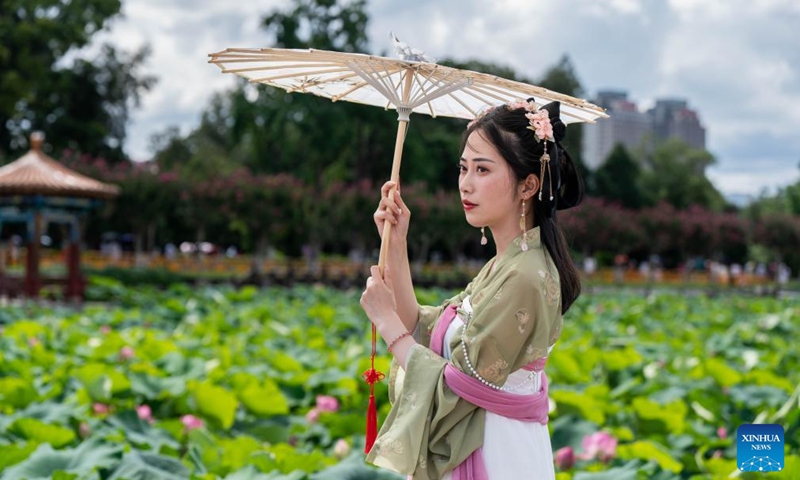 A woman enjoys lotus flowers at Daguan Park in Kunming, southwest China's Yunnan Province, July 7, 2024. (Xinhua/Hu Chao)