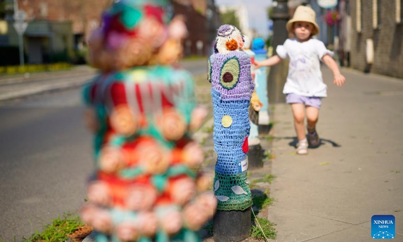 A girl walks past bollards adorned with woven fabrics by artisans in Praga district in Warsaw, capital of Poland, July 11, 2024. The Praga district is renowned for its vibrant cultural and creative atmosphere, with numerous galleries, museums, and designer studios. (Photo: Xinhua)