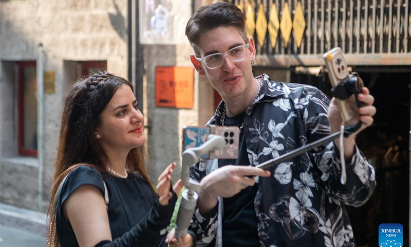 Ilia Anfilatov (R) and Syyra Alee take videos at a cultural park in Yuzhong District of southwest China's Chongqing Municipality, July 12, 2024. International students Ilia Anfilatov from Russia and Syyra Alee from Pakistan have been studying at Southwest University in Chongqing for over a year.