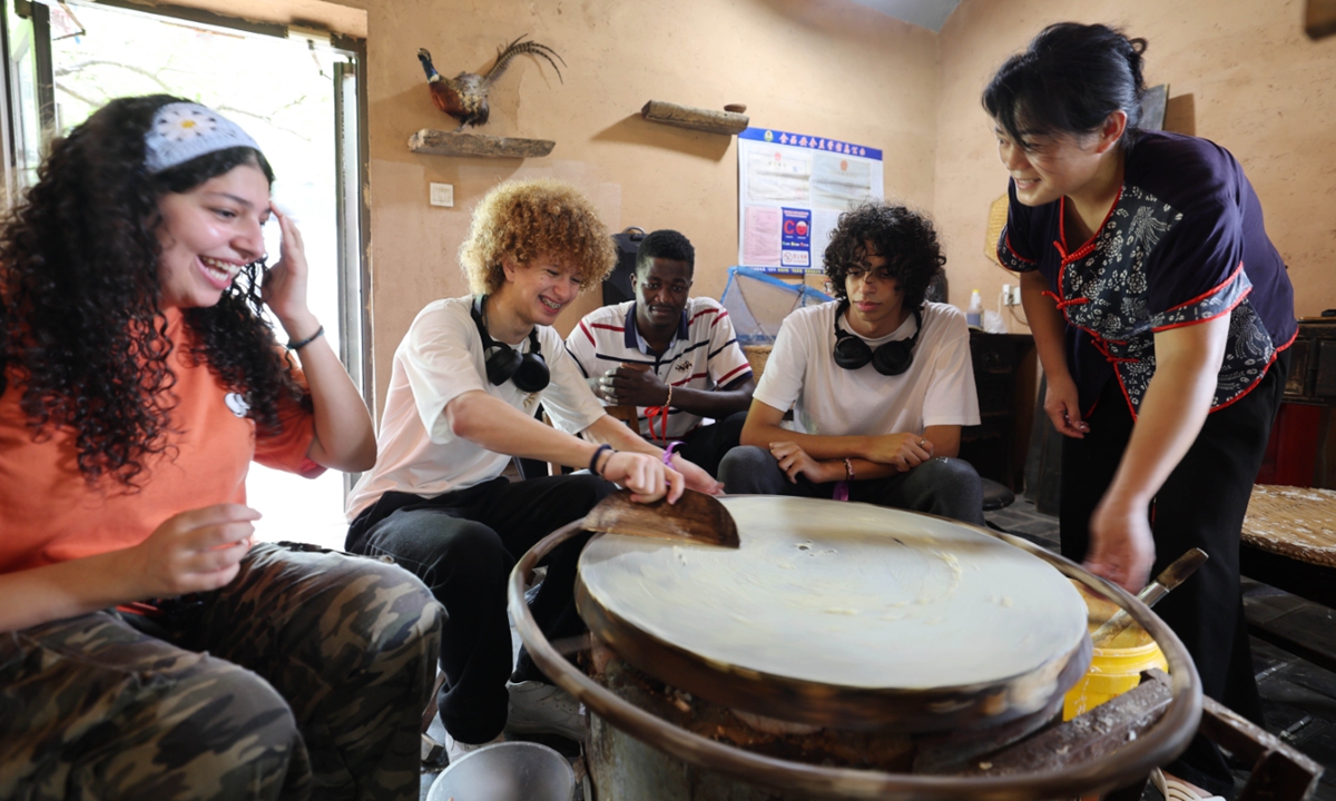 Foreign students learn to make fried pancakes under the guidance of a local villager in Yinan county, East China's Shandong Province, on July 21, 2024. More than 30 foreign students came to the village to experience traditional Chinese crafts and intangible cultural heritage projects such as straw weaving and making fried pancakes, immersing themselves in the charm of rural Chinese culture. Photo: VCG