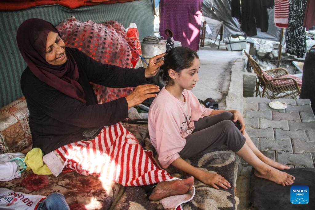 A Palestinian woman who returned home takes care of her child at a temporary tent over the rubble of a destroyed house in Beit Lahia town in northern Gaza on July 21, 2024. (Photo: Xinhua)