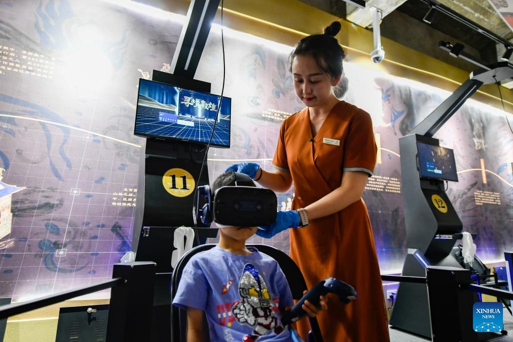 A staff member helps a boy use virtual reality (VR) equipment to visit the Mogao Grottoes in Dunhuang, northwest China's Gansu Province, July 22, 2024. A digital exhibition utilizing technologies as 3D modeling and VR devices is held to help visitors have an immersive impression of the culture of Dunhuang. (Photo: Xinhua)