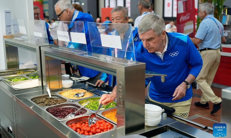 IOC President Thomas Bach (front) tries food from a salad bar while touring the Olympic Village ahead of the Paris 2024 Olympic Games, on July 22, 2024, in Paris, France. (Photo by David Goldman/POOL/Xinhua)