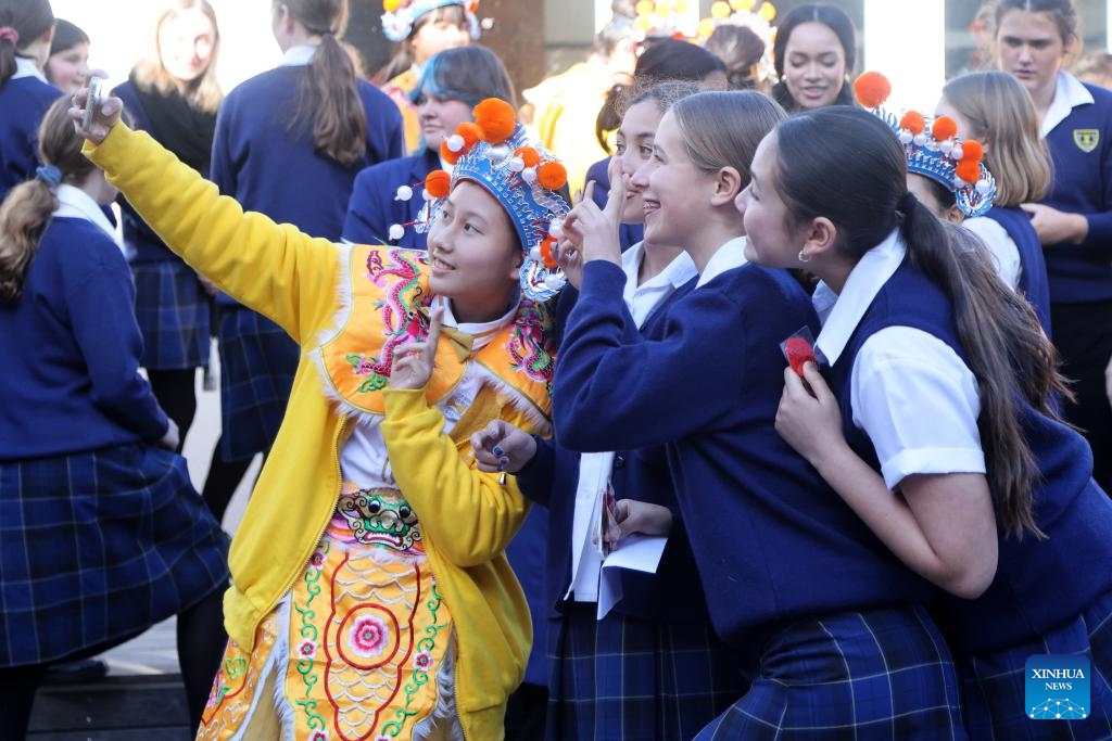 A member of China's Guangzhou Opera House Children's Choir and students of Wellington East Girls' College take selfies in Wellington, New Zealand, July 24, 2024. Members of Guangzhou Opera House Children's Choir visited Wellington East Girls' College in New Zealand on Wednesday, and held a joint concert with the high school's choir at the opening ceremony of the new semester of the school. (Photo: Xinhua)