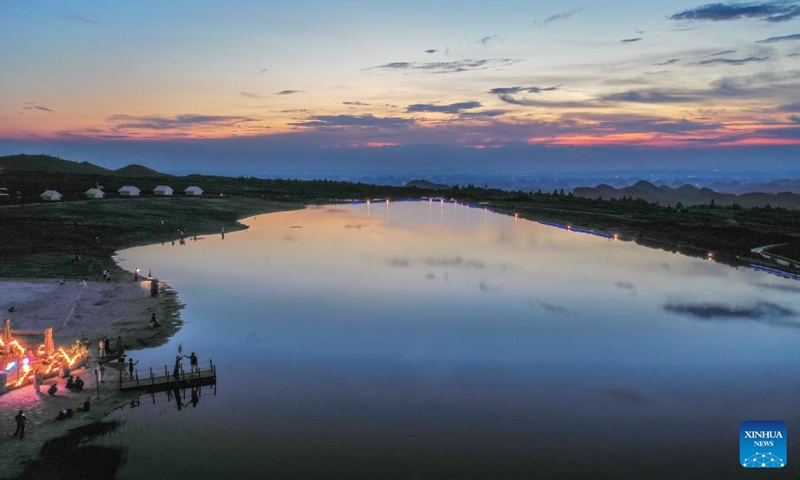 An aerial drone photo taken on July 25, 2024 shows tourists enjoying sunset glow at the Zimei Lake scenic spot in Jinxing Village, Longshan Town, Longli County, southwest China's Guizhou Province. During summer vacation, Longli County has become a popular destination for tourists to escape the sweltering summer heat. In recent years, local authorities have promoted the upgrading of the rural tourism, which attracts more tourists to visit. Photo: Xinhua