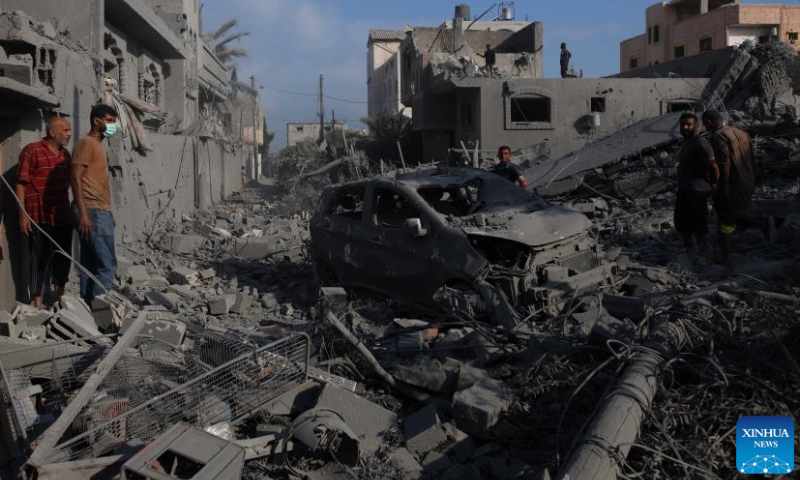 People stand among the rubble after an Israeli airstrike in the Nuseirat refugee camp, central Gaza Strip, on Aug. 12, 2024. The Palestinian death toll from ongoing Israeli attacks on the Gaza Strip has risen to 39,897, Gaza-based health authorities said in a statement on Monday. (Photo by Marwan Dawood/Xinhua)