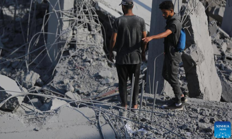 People stand among the rubble after an Israeli airstrike in the Nuseirat refugee camp, central Gaza Strip, on Aug. 12, 2024. The Palestinian death toll from ongoing Israeli attacks on the Gaza Strip has risen to 39,897, Gaza-based health authorities said in a statement on Monday. (Photo by Marwan Dawood/Xinhua)