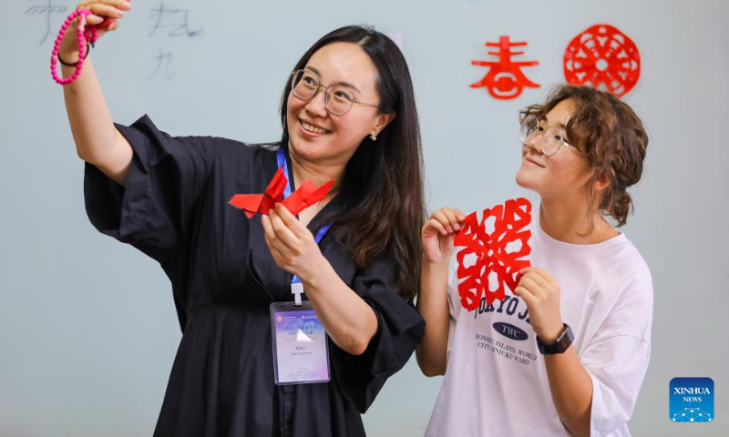 A Russian student shows her paper-cut work while posing for selfies with a Chinese teacher at Qingdao Hengxing University in Qingdao, east China's Shandong Province, Aug. 12, 2024. A summer camp themed on Chinese learning was recently held in Qingdao, with activities for 12 Russian students featuring traditional intangible cultural heritages. (Photo: Xinhua)