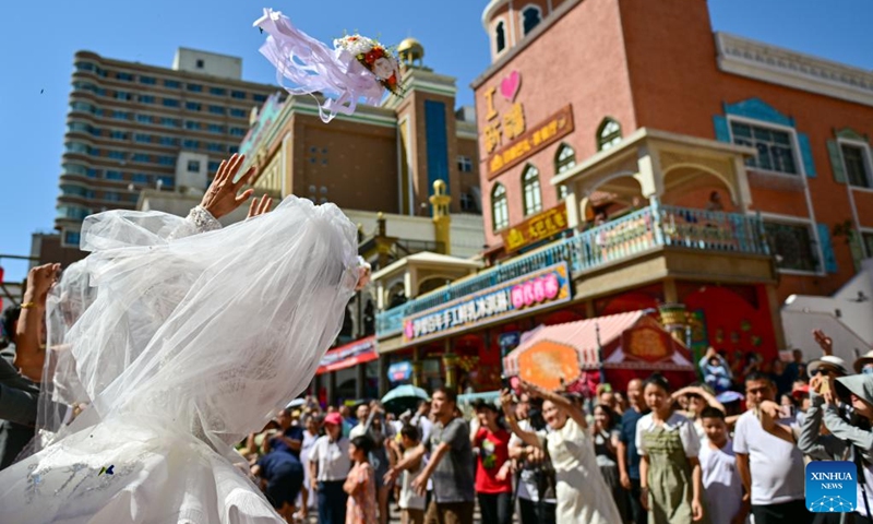 A bride throws a bouquet during a group wedding at the Xinjiang International Grand Bazaar in Urumqi, northwest China's Xinjiang Uygur Autonomous Region, Aug. 10, 2024. The group wedding was held here on Saturday to mark the Qixi Festival, also known as Chinese Valentine's Day. Photo: Xinhua