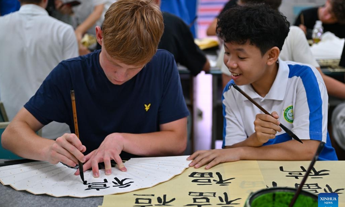 A Chinese student teaches a German student Chinese calligraphy at a school in Haikou, south China's Hainan Province, Aug. 7, 2024. German students attending a Sino-German U16 football tournament visited a middle school in Haikou for a study tour on Wednesday. (Photo: Xinhua)