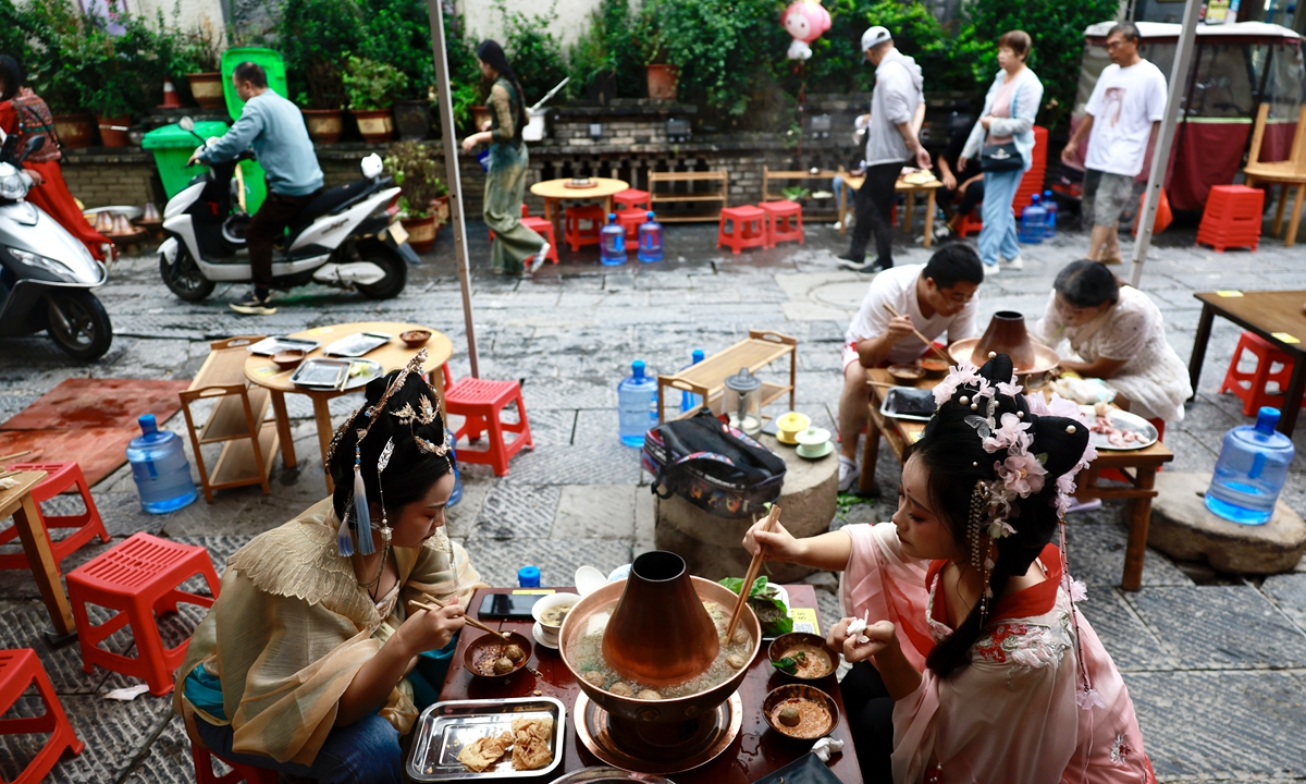 Two young girl dressed in traditional Chinese costumes taste local snacks on a street in Luoyang, Central China's Henan Province, in August 2023. Photo: Li Hao/GT