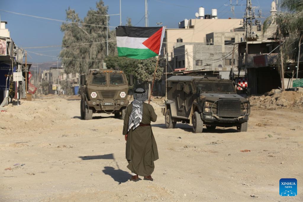 A man with a Palestinian flag stands in front of Israeli military vehicles on a street during a military operation in the Nour Shams refugee camp, east of the city of Tulkarm in the West Bank, on Aug. 29, 2024. According to Palestinian and Israeli sources, the Israeli army on Wednesday launched a large-scale military operation in Tulkarm, Jenin, and Tubas refugee camps in an attempt to arrest wanted persons accused of involvement in operations against Israel. (Photo: Xinhua)