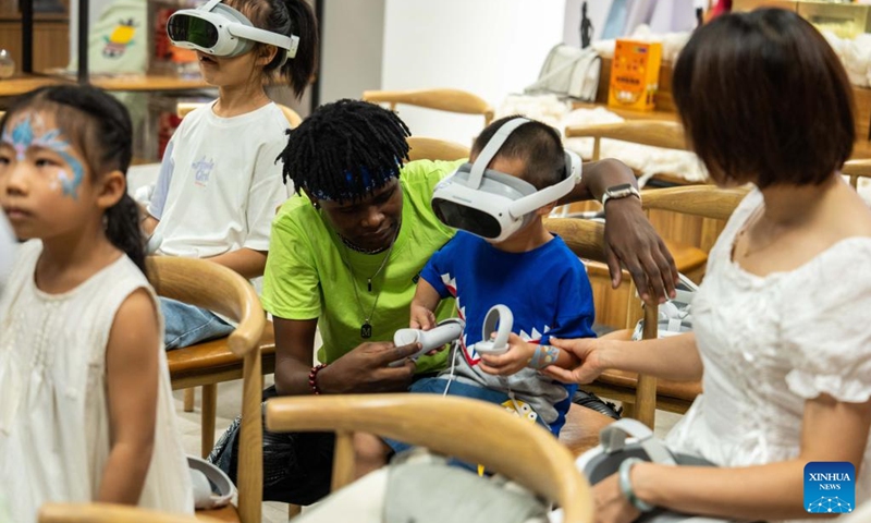 A volunteer helps a kid to put on VR device during a hands-on experience session at the Mali pavilion of a permanent exhibition hall of the China-Africa Economic and Trade Cooperation Promotion Innovation Demonstration Park in Changsha, central China's Hunan Province, Aug. 30, 2024. Various activities promoting youth communication between China and Africa were organized here during the summer vacation. With the help of African volunteers from local universities, Chinese students were able to feel the charm of African culture by learning traditional African dance, music, folk arts, and making immersive tours of African customs via VR devices. Photo: Xinhua