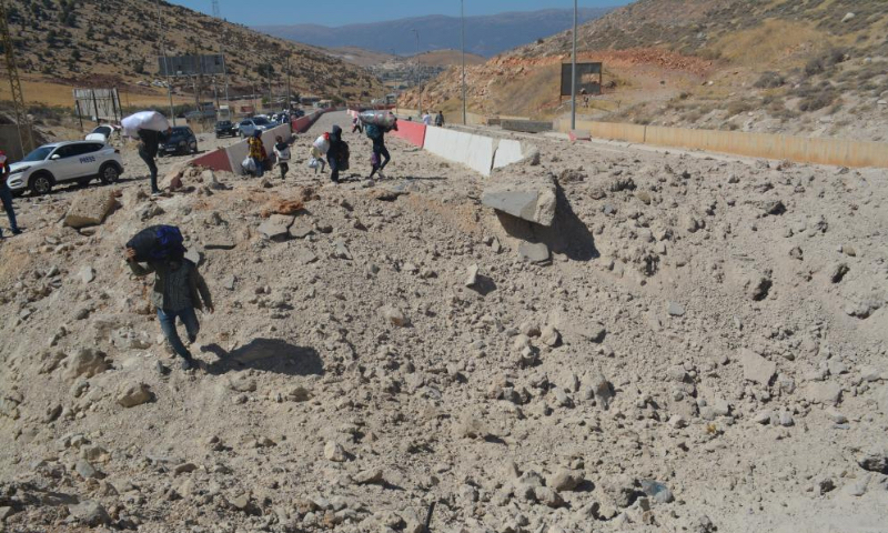 Displaced people from Lebanon cross a destroyed road caused by an Israeli airstrike near the Masnaa Border Crossing, Lebanon, Oct. 4, 2024. The Syrian Foreign Ministry denounced an Israeli airstrike on the Syria-Lebanon border on Friday, accusing Israel of targeting civilians and vital infrastructure in its ongoing campaign of aggression. According to the ministry, the airstrike hit the Jdeidat Yabous crossing, also known as the Masnaa crossing in Lebanon, a key transit route used by tens of thousands of Lebanese refugees and Syrian citizens fleeing the Israeli assault in Lebanon. (Photo by Taher Abu Hamdan/Xinhua)