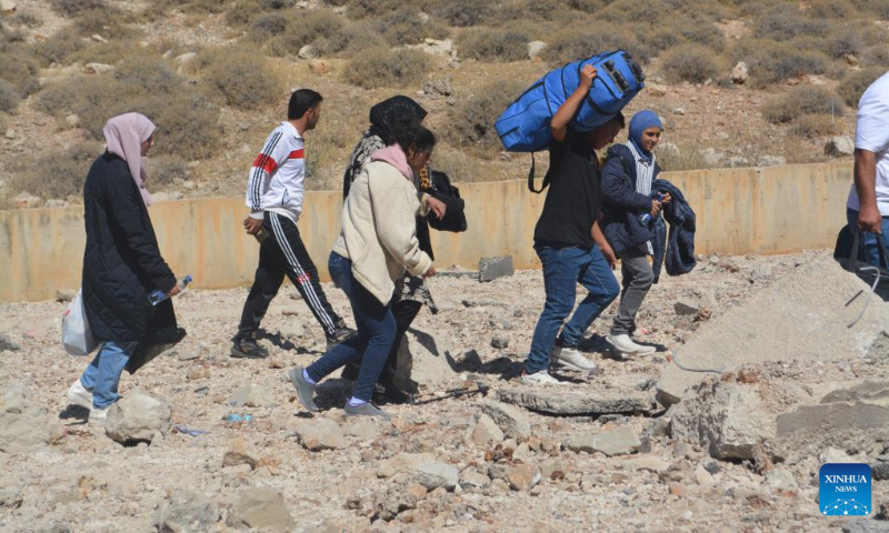 Displaced people from Lebanon cross a destroyed road caused by an Israeli airstrike near the Masnaa Border Crossing, Lebanon, Oct. 4, 2024. The Syrian Foreign Ministry denounced an Israeli airstrike on the Syria-Lebanon border on Friday, accusing Israel of targeting civilians and vital infrastructure in its ongoing campaign of aggression. According to the ministry, the airstrike hit the Jdeidat Yabous crossing, also known as the Masnaa crossing in Lebanon, a key transit route used by tens of thousands of Lebanese refugees and Syrian citizens fleeing the Israeli assault in Lebanon. (Photo by Taher Abu Hamdan/Xinhua)