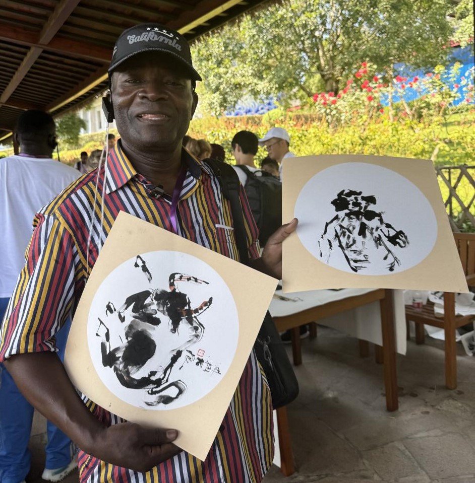 Emile Gankama, editorial director of Les Depeches De Brazzaville, Republic of the Congo, shows a piece of painting (right) co-finished by himself and Lin Xu, an inheritor of Mount Emei finger painting. (People's Daily/Xu Hangyan)