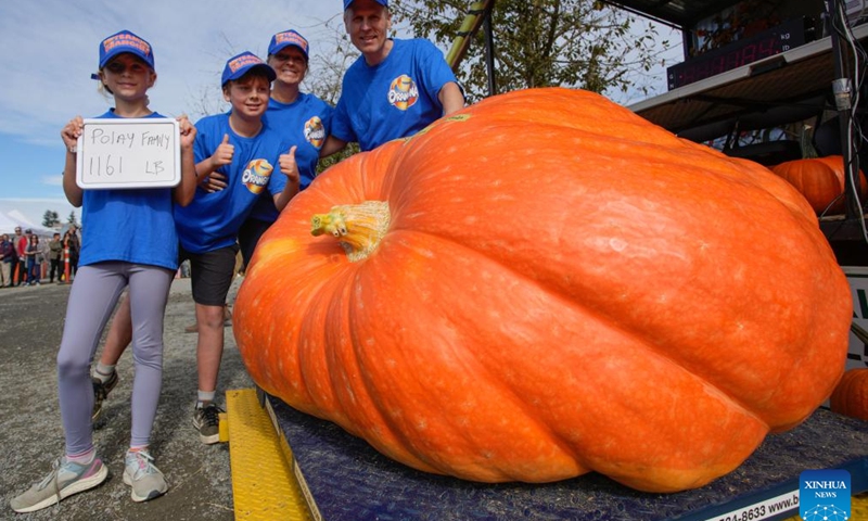 Mike Polay (R) poses for photos with his winning pumpkin weighing 1,161 pounds alongside family members during the 2024 Giant Pumpkin Weigh-Off competition in Langley, British Columbia, Canada, Oct. 5, 2024. The annual province-wide giant pumpkin weigh-off competition returned to Langley on Saturday, drawing dozens of growers to compete. (Photo by Liang Sen/Xinhua)