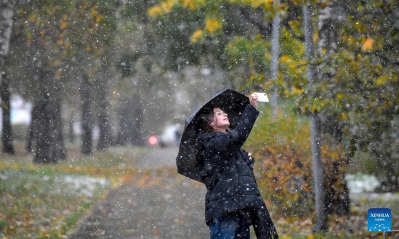 A girl takes pictures during snowfall in Moscow, Russia, on Oct. 14, 2024. (Photo: Xinhua)