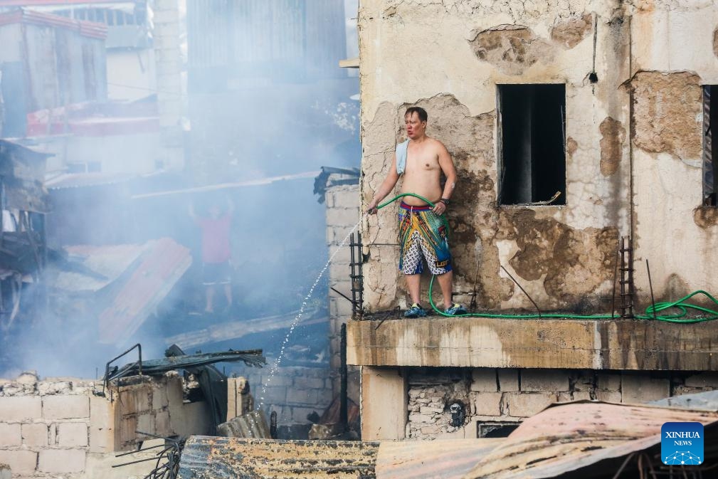 A resident uses a water hose at his charred home after a fire at a slum area in Manila, the Philippines, on Oct. 15, 2024. (Photo: Xinhua)