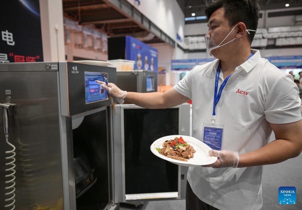 A staff member prepares food by a robot chef during the 2nd Hainan International Tropical Food Supply Chain Expo in Haikou, south China's Hainan Province, Oct. 17, 2024. The 2nd Hainan International Tropical Food Supply Chain Expo kicked off here Thursday. (Photo: Xinhua)