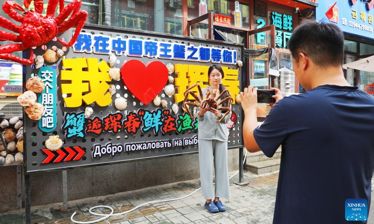 A tourist poses for photos with an installation themed on king crabs in Hunchun, northeast China's Jilin Province, Sept. 21, 2024. Hunchun City of northeast China's Jilin Province has a nickname capital of king crabs among netizens. Every day, trucks fully loaded with fresh seafood imports enter the city via a land checkpoint bordering Russia. The Russian king crab, also known as the Kamchatka crab, is the star product. (Photo: Xinhua)