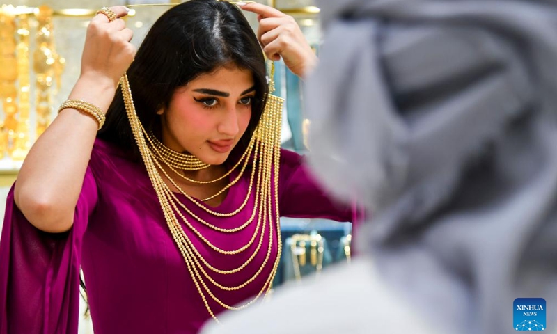 A woman tries on a golden necklace at a stall during the ASJAD Jewelry Exhibition at Alhazm Mall in Doha, Qatar, Oct. 24, 2024. The exhibition is held here from Oct. 24 to 29. (Photo: Xinhua)