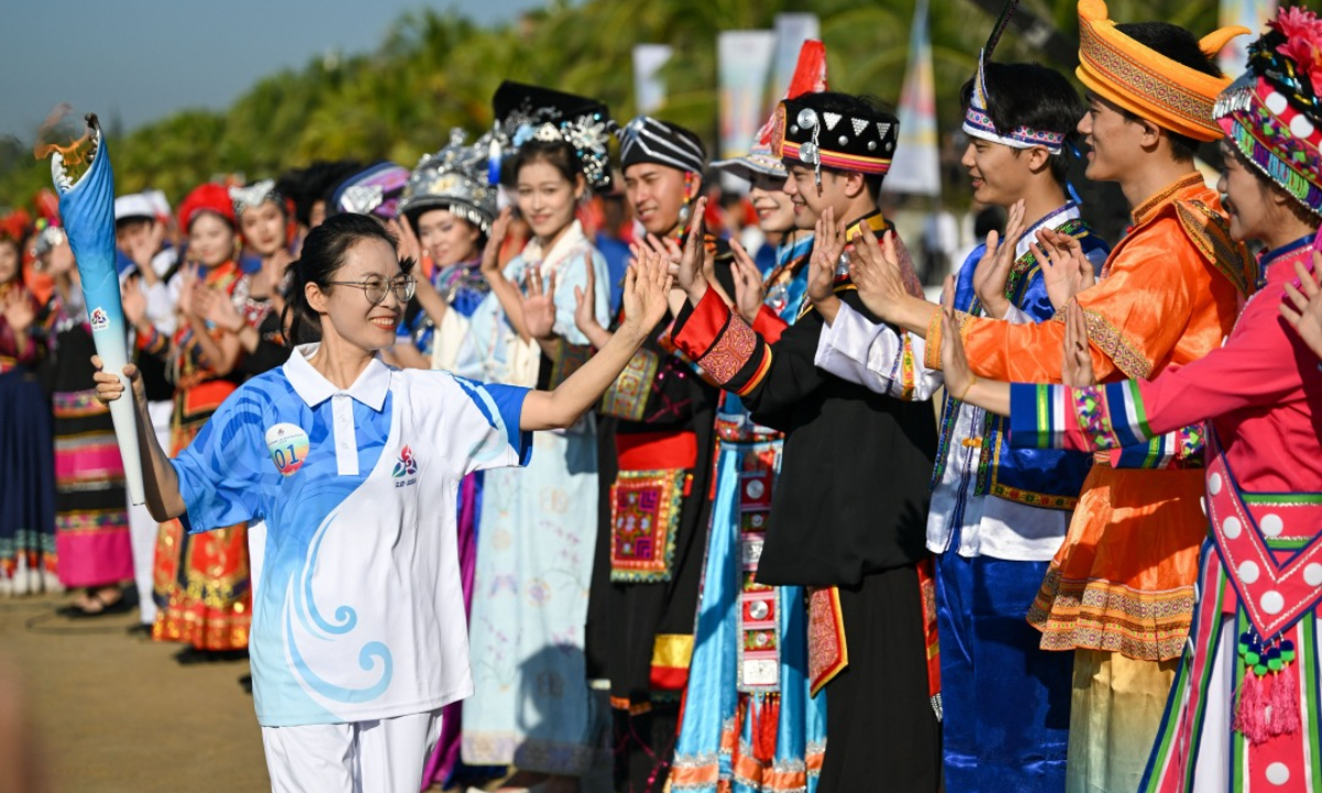 A torchbearer for the National Traditional Games of Ethnic Minorities of the People's Republic of China (left) interacts with the audience dressed in ethnic costumes during the torch relay in Sanya, South China's Hainan Province, on November 17, 2024. Photo: Courtesy of the organizers