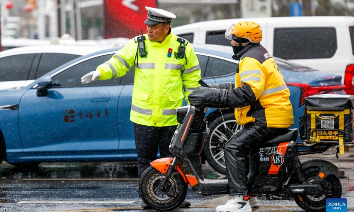 A traffic police officer reminds a deliveryman to pay attention to slippery road conditions in Urumqi, northwest China's Xinjiang Uygur Autonomous Region, Nov. 14, 2024. A cold front has ushered in significant drop in temperature and snowfall across Xinjiang. (Photo: Xinhua)