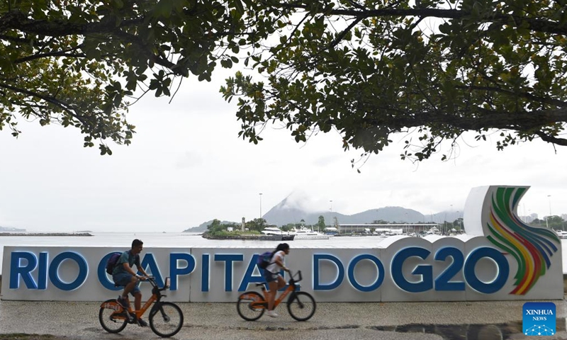 People ride bicycles past a G20 logo near the main venue of the 19th G20 summit in Rio de Janeiro, Brazil, Nov. 16, 2024. The 19th G20 summit is scheduled from Nov. 18 to 19 in Rio de Janeiro. (Photo by Lucio Tavora/Xinhua)