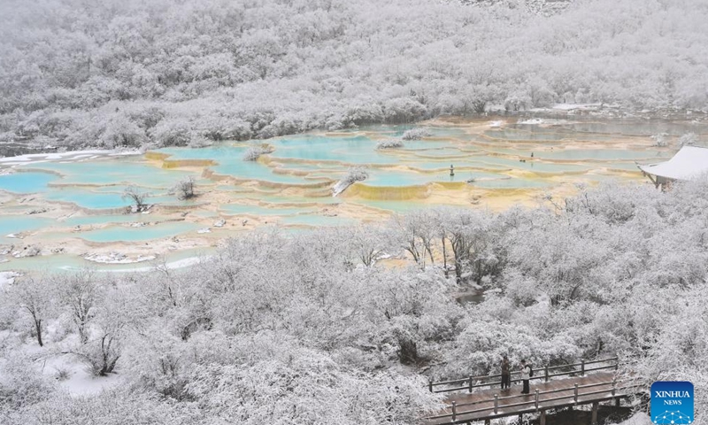 This photo taken on Nov. 18, 2024 shows tourists viewing a colorful pond cluster at Huanglong scenic area after snow in Tibetan-Qiang Autonomous Prefecture, southwest China's Sichuan Province. (Photo: Xinhua)