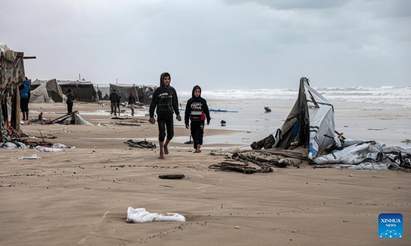 Displaced people walk past a tent damaged in heavy rain in the Mawasi area of Khan Younis, southern Gaza Strip, on Nov. 25, 2024. UN humanitarians said on Monday they and their partners have been evaluating flood damage in a response to multiple sites for displaced Gazans hit by heavy weekend rainfall. (Photo: Xinhua)