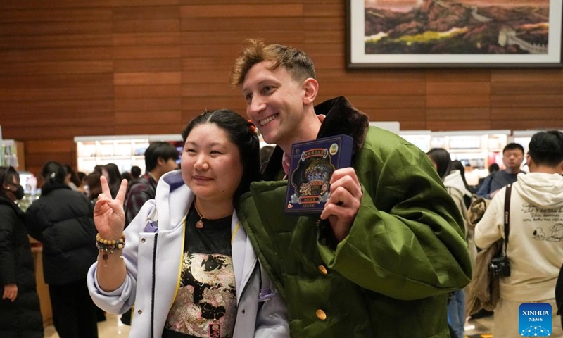 Evan Kail (front, R) poses for a photo with a tourist after receiving a cultural creative magnet at the National Museum of China in Beijing, capital of China, Nov. 19, 2024. (Xinhua/Ju Huanzong)