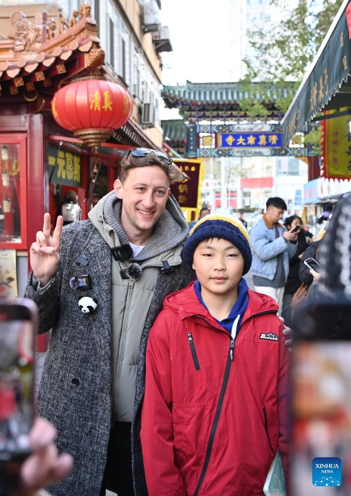 Evan Kail (L), a pawnshop manager from the United States, poses for photos with a local child when visiting a cultural street in north China's Tianjin Municipality, Nov. 28, 2024.