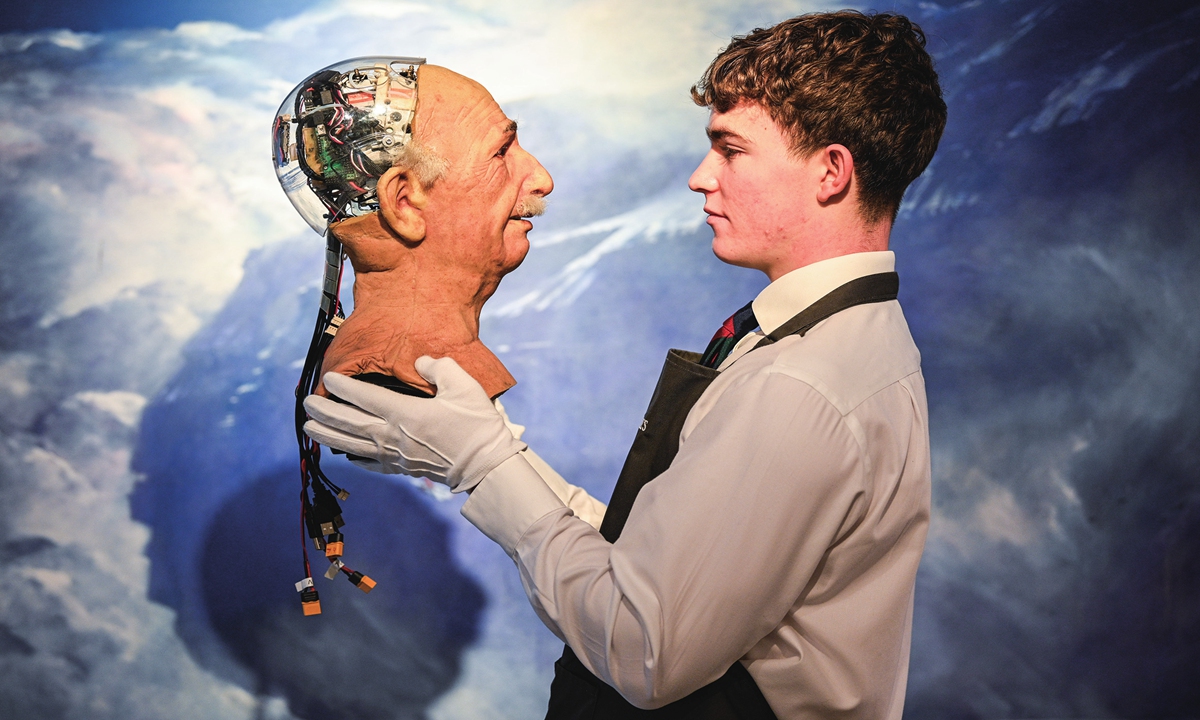 An arts handler from Christie's poses with a robotic head resembling Einstein on November 29, 2024 in London, England. Highlights of these pre-Christmas sales include the only surviving landscape in oil by Van Dyck, original Paddington bear drawings by illustrator Peggy Fortnum, a signed Beethoven manuscript and several paintings by Rembrandt. Photo: VCG 