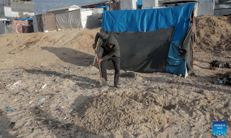 Odai Olaiwa tidies up the area around the tent he lives on the seaside in the city of Deir al-Balah in central Gaza Strip, Nov. 28, 2024. (Photo: Xinhua)