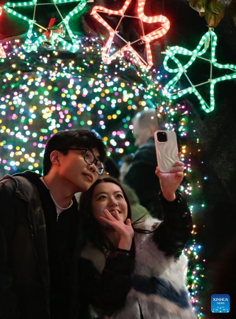 People pose for a selfie in front of the Christmas lights during the Lights of Hope lighting ceremony in Vancouver, British Columbia, Canada, Nov. 27, 2024. Lights of Hope is one of Vancouver's largest annual Christmas fundraiser, showcasing over 200,000 colourful lights illuminating St. Paul's Hospital. (Photo by Liang Sen/Xinhua)