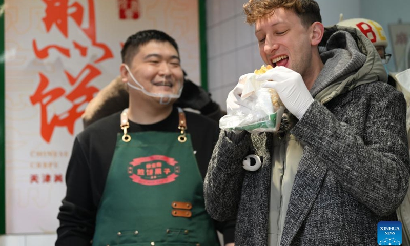 Evan Kail (R), a pawnshop manager from the United States, tries the local street food Jianbing Guozi in north China's Tianjin Municipality, Nov. 28, 2024.