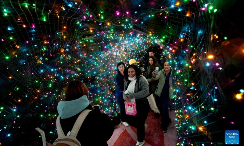 People pose for photos with the Christmas lights during the Lights of Hope lighting ceremony in Vancouver, British Columbia, Canada, Nov. 27, 2024. Lights of Hope is one of Vancouver's largest annual Christmas fundraiser, showcasing over 200,000 colourful lights illuminating St. Paul's Hospital. (Photo by Liang Sen/Xinhua)