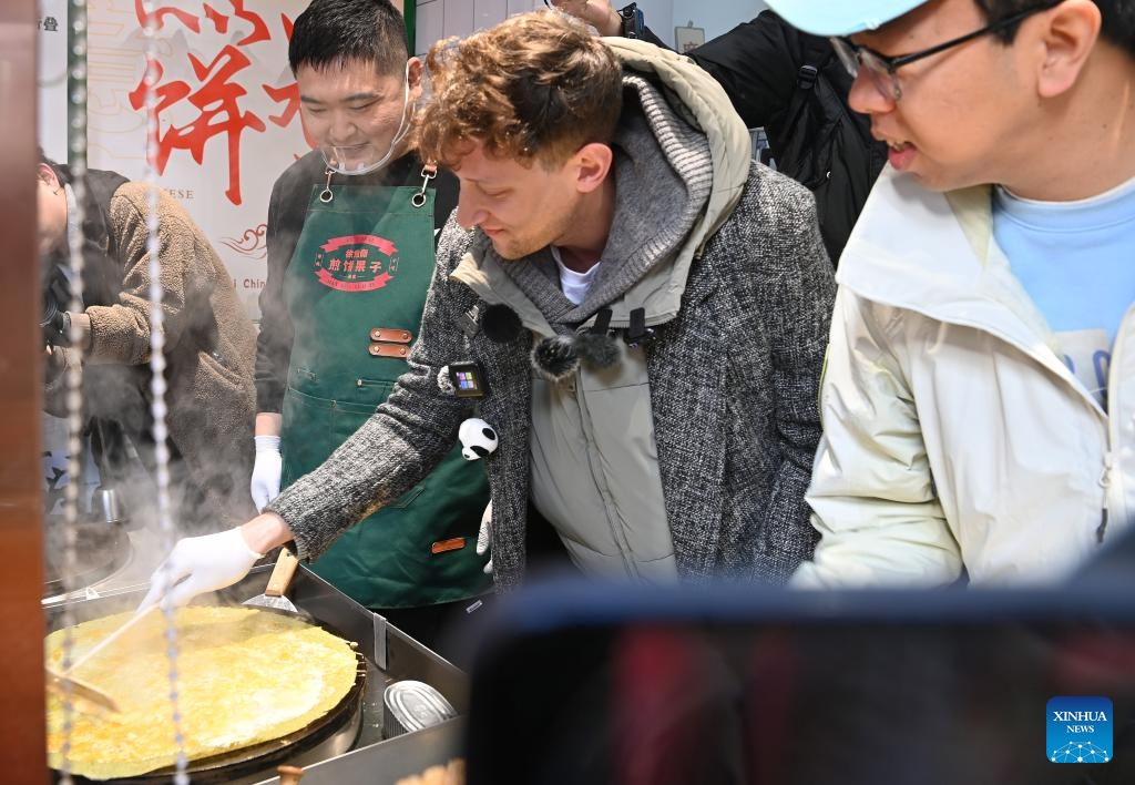 Evan Kail (C), a pawnshop manager from the United States, learns to make the local street food Jianbing Guozi in north China's Tianjin Municipality, Nov. 28, 2024.