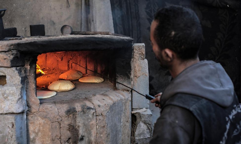 A Palestinian bakes bread with an old clay oven in the southern Gaza Strip city of Khan Younis, on Dec. 2, 2024. The UN agency for Palestine refugees decided on Sunday to pause aid delivery through the Kerem Shalom crossing, a main entry point for humanitarian aid into the Gaza Strip, citing ongoing safety concerns along the route. This was expected to further deteriorate the supply of daily necessities including flour for bread in the Gaza Strip. (Photo: Xinhua)