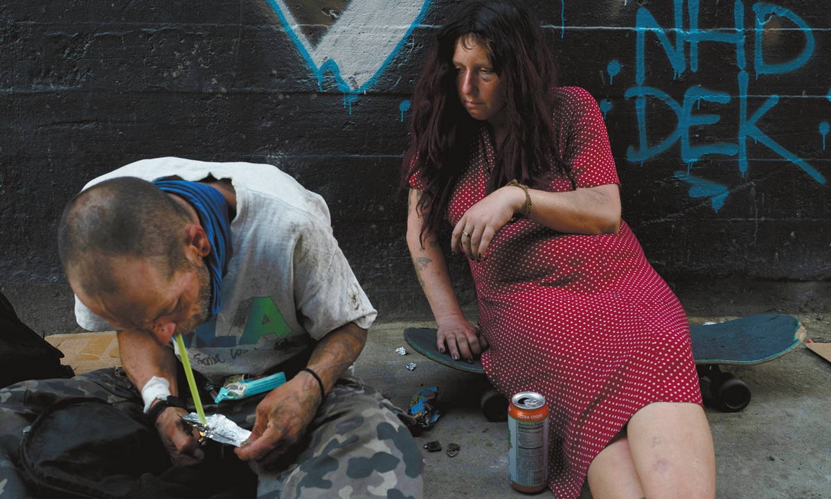 A fentanyl user sits on her skateboard while another drug user inhales an unidentified substance in Los Angeles, the US. Photo: VCG 