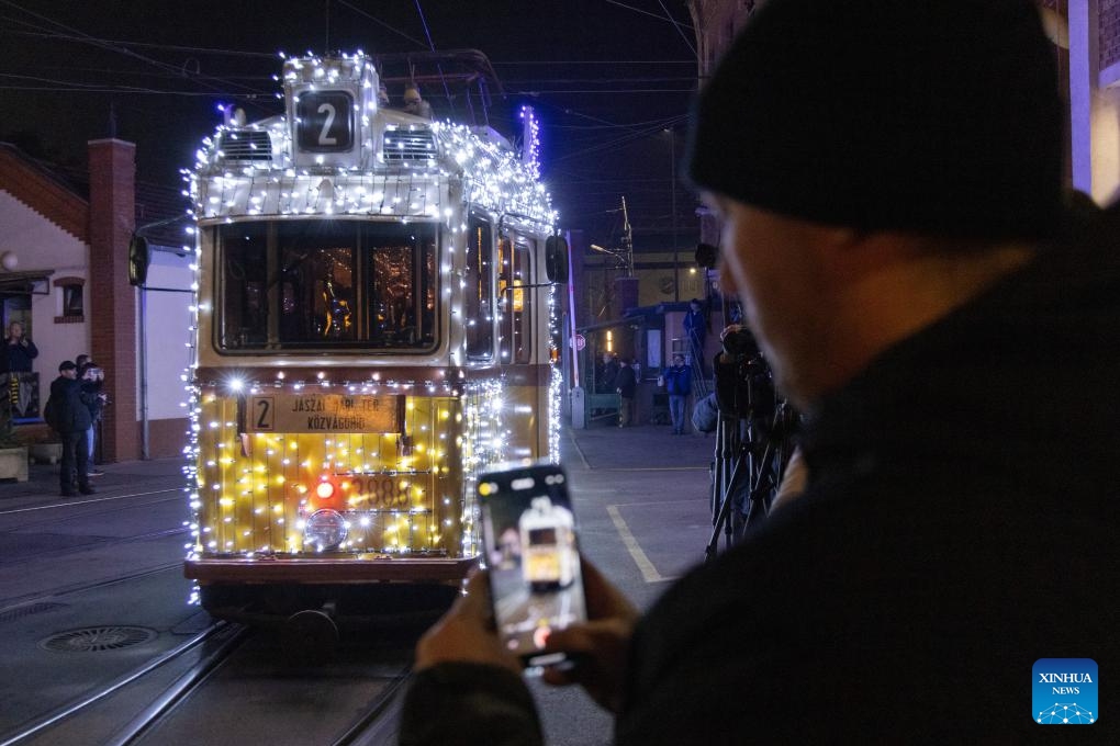 A man takes photos of a Christmas light-decorated tram in Budapest, Hungary on Dec. 2, 2024. (Photo: Xinhua)