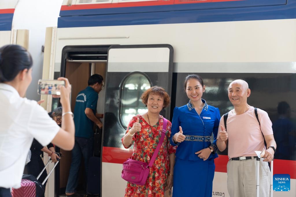 Passengers pose for a photo with a train of the China-Laos Railway at the Vientiane Station in Vientiane, Laos, Dec. 2, 2024. The China-Laos Railway has emerged as a catalyst for regional economic growth three years after its launch, China's railway operator said on Tuesday. Offering a safe and sustainable operation, the railway had handled over 43 million passenger trips and transported 48.3 million tonnes of cargo as of Monday, according to the China State Railway Group Co., Ltd. (Photo: Xinhua)