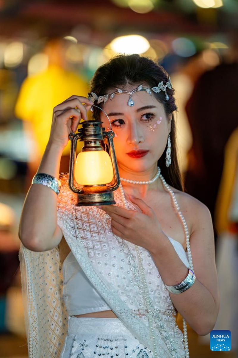 A tourist poses for photos at the Starlight Night Market in Jinghong City of Xishuangbanna Dai Autonomous Prefecture, southwest China's Yunnan Province, Dec. 7, 2024. The night market is a destination to experience the customs of Dai ethnic group. Photo: Xinhua