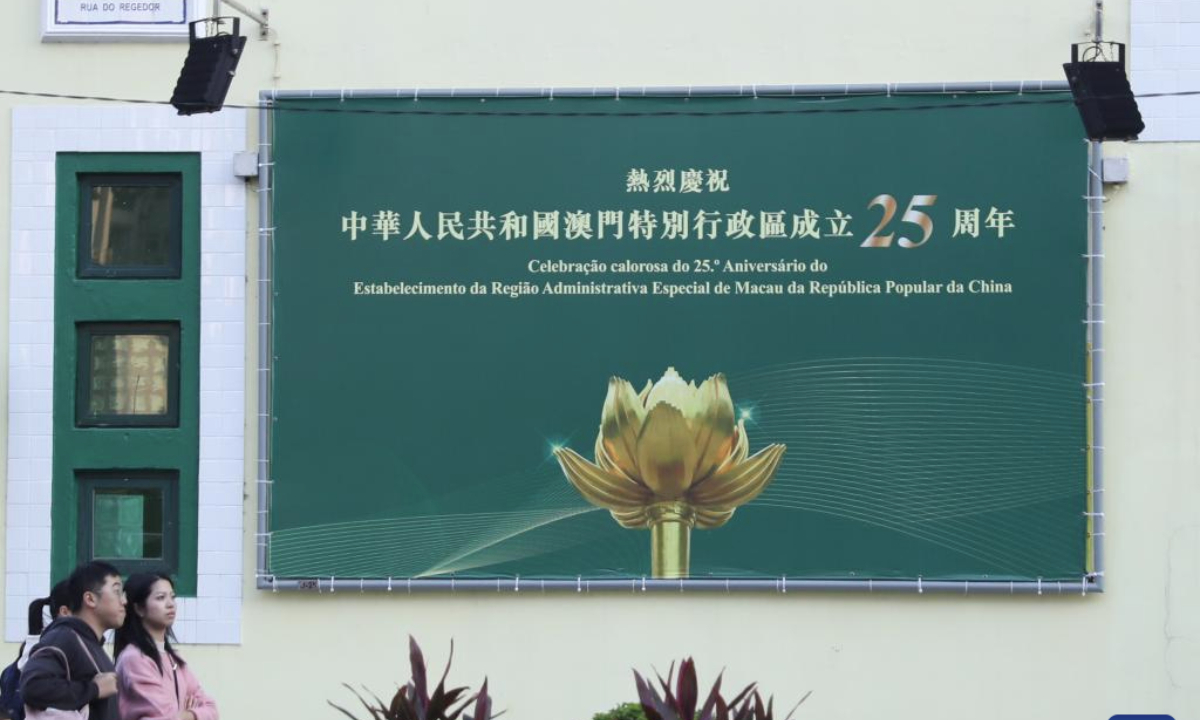 People walk past a celebration poster in Macao, south China, Dec. 17, 2024. The streets of Macao have been adorned by festive decorations, as the city is set to mark the 25th anniversary of its return to the motherland. (Xinhua/Yao Qilin)

